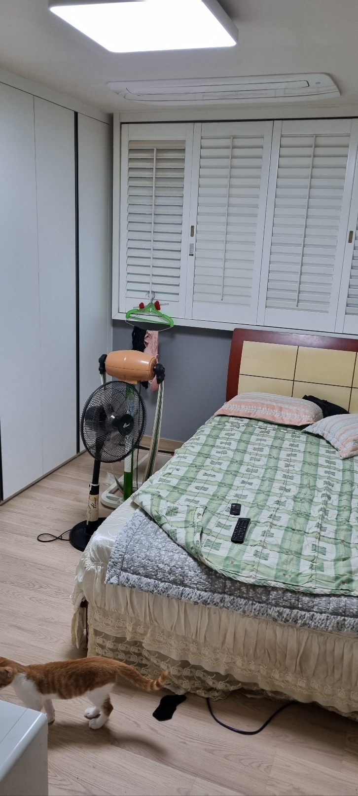 천장 조명과 에어컨, 흰 붙박이장과 침대가 보이는 방