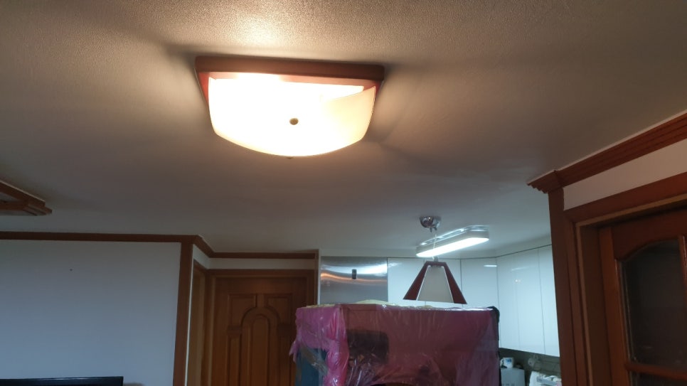 조명이 켜진 흰 천장과 갈색 몰딩, 분홍색 비닐로 보양한 물건