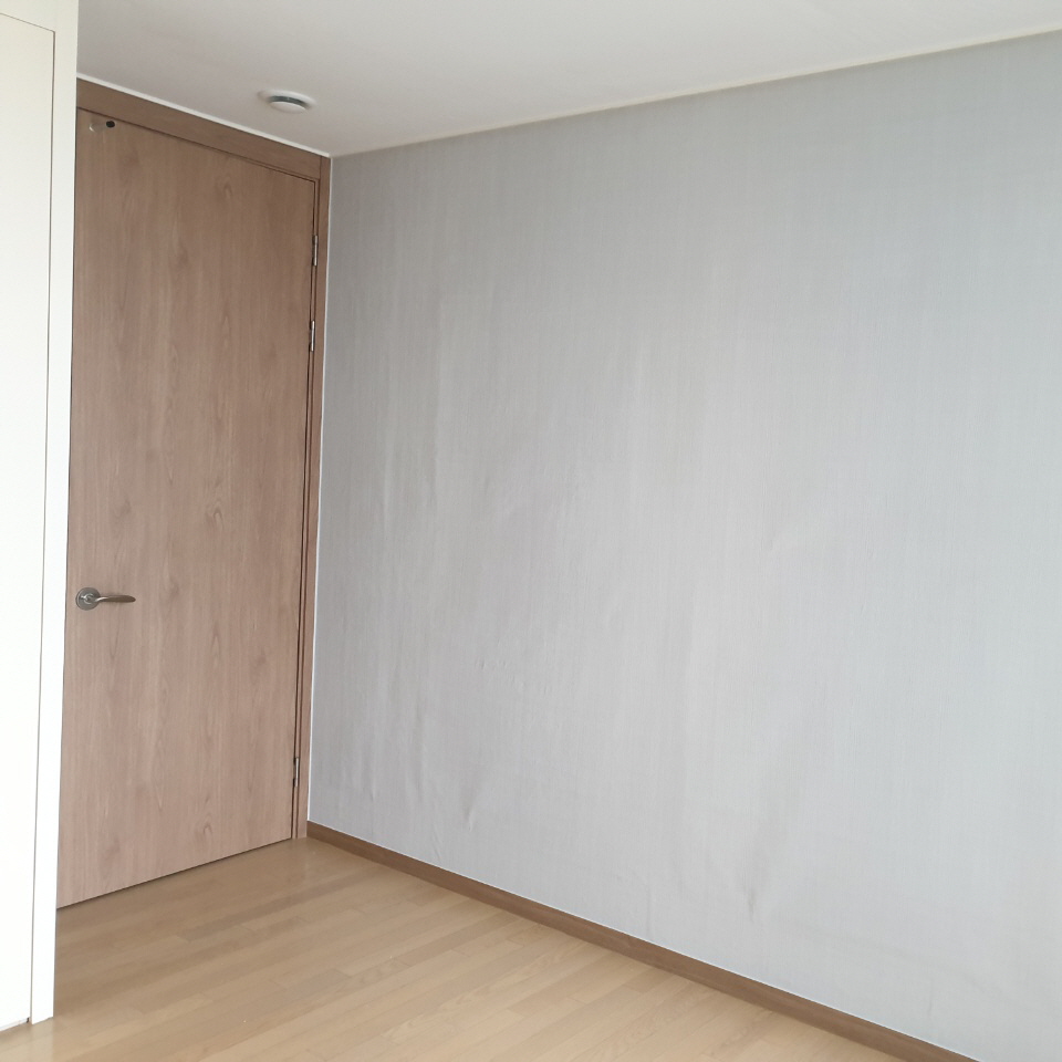 닫힌 목재 문과 세로 굴곡·하단 주름이 보이는 회색 벽면