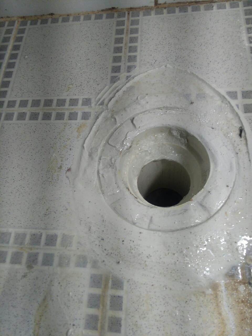 배수구 둘레와 타일 가장자리에 흰색 재료가 발라진 모습
