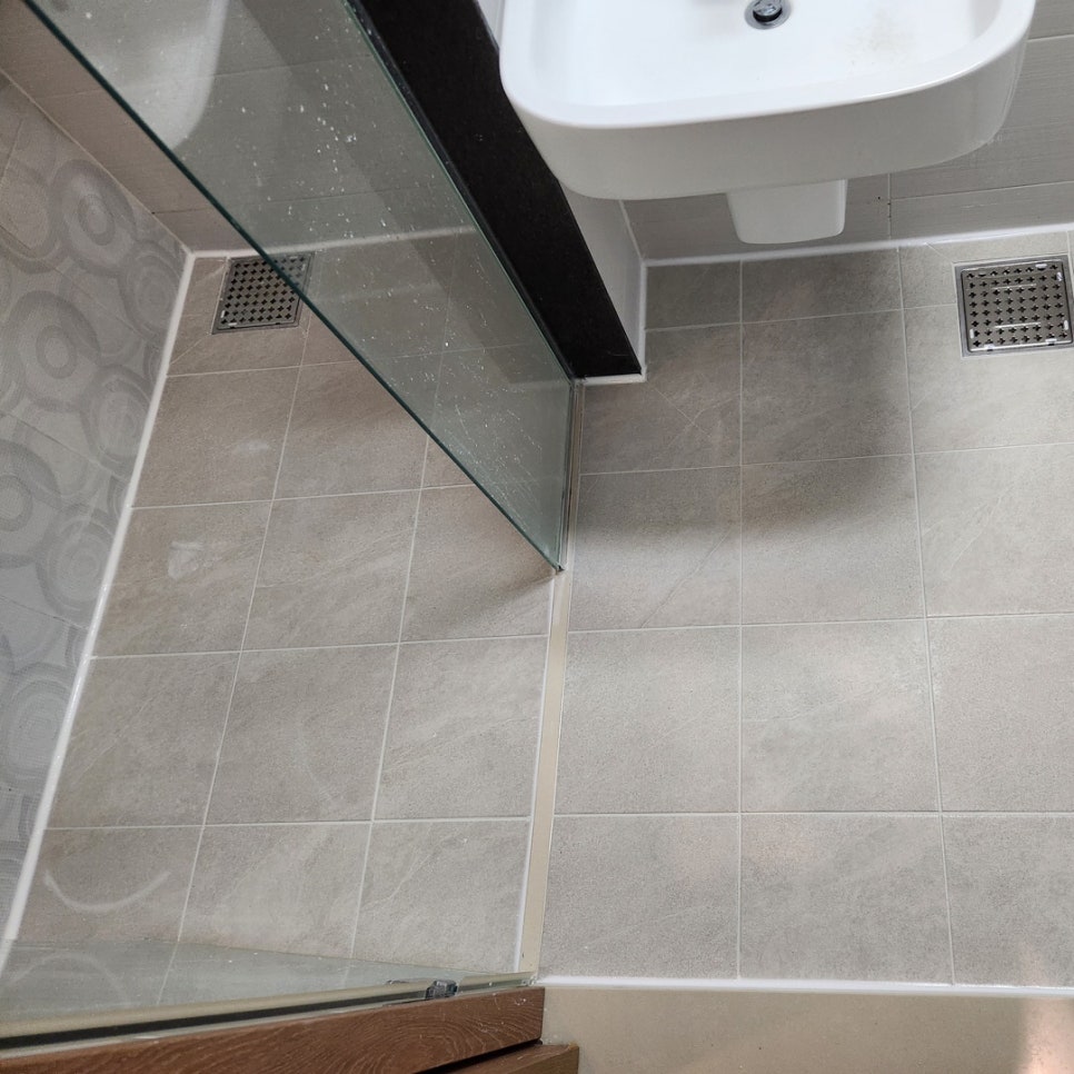 유리 칸막이로 나뉜 샤워 공간과 세면대 쪽 바닥의 두 배수구