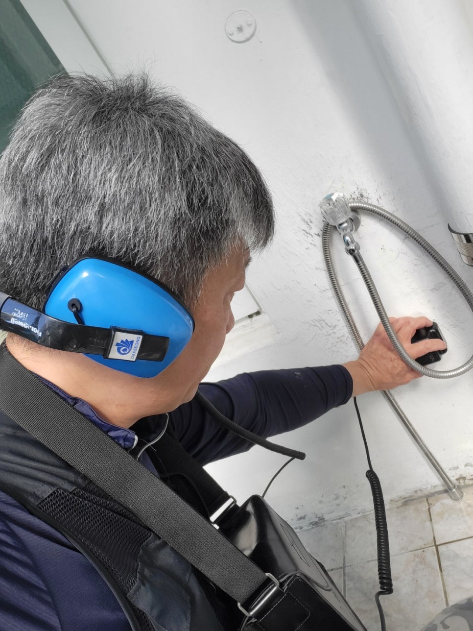 수전 아래 금속 호스 주변 벽면에 유선 센서를 대고 점검하는 작업자
