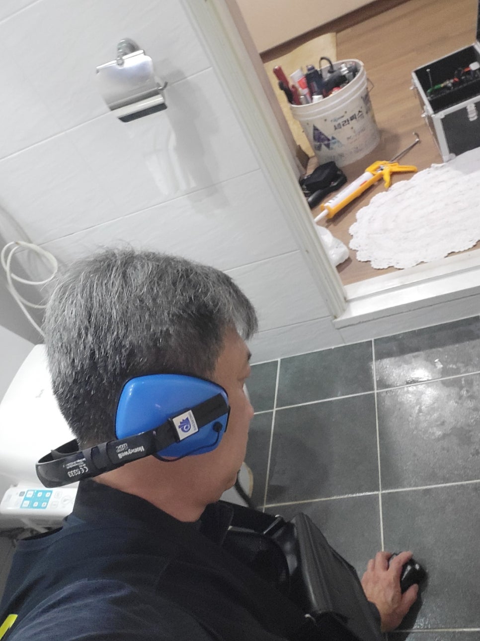 욕실 출입구 쪽 바닥 타일을 장비로 점검하는 작업자