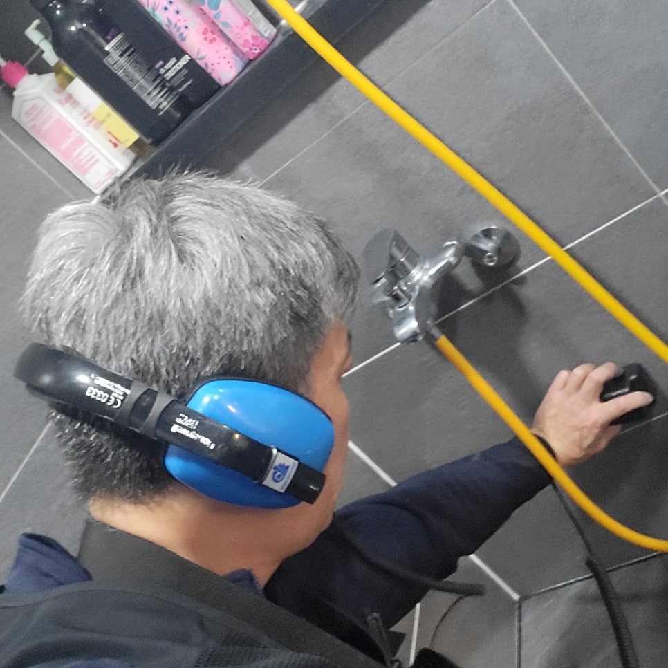 수전 오른쪽 아래 벽타일에 검은 장치를 대는 작업자