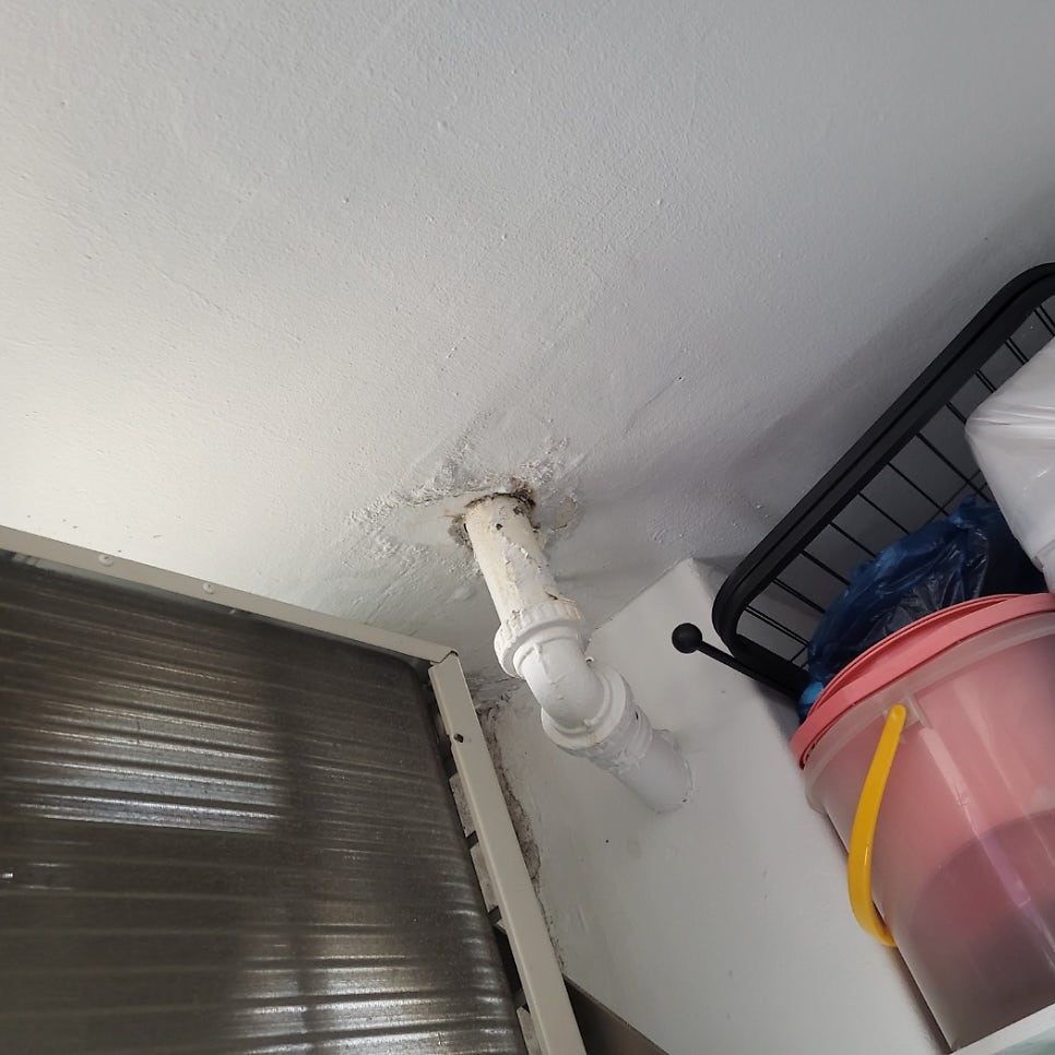 천장 관통부에서 굽어 이어지는 흰색 배관과 주변 도장 손상