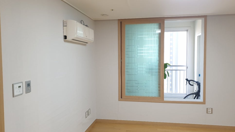 벽걸이 에어컨과 목재 색 창틀이 있는 밝은 벽면과 목재 무늬 바닥