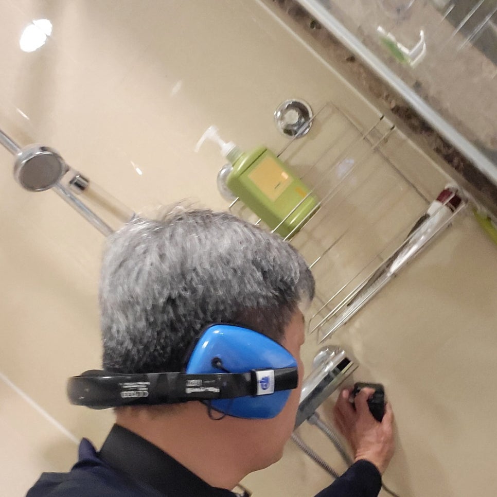 샤워 수전 옆 벽면에 검은 장치를 대고 있는 작업자