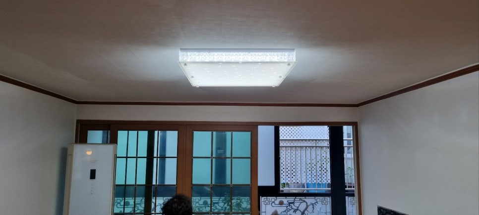 사각 조명과 갈색 몰딩이 있는 거실 천장, 창문과 스탠드형 에어컨