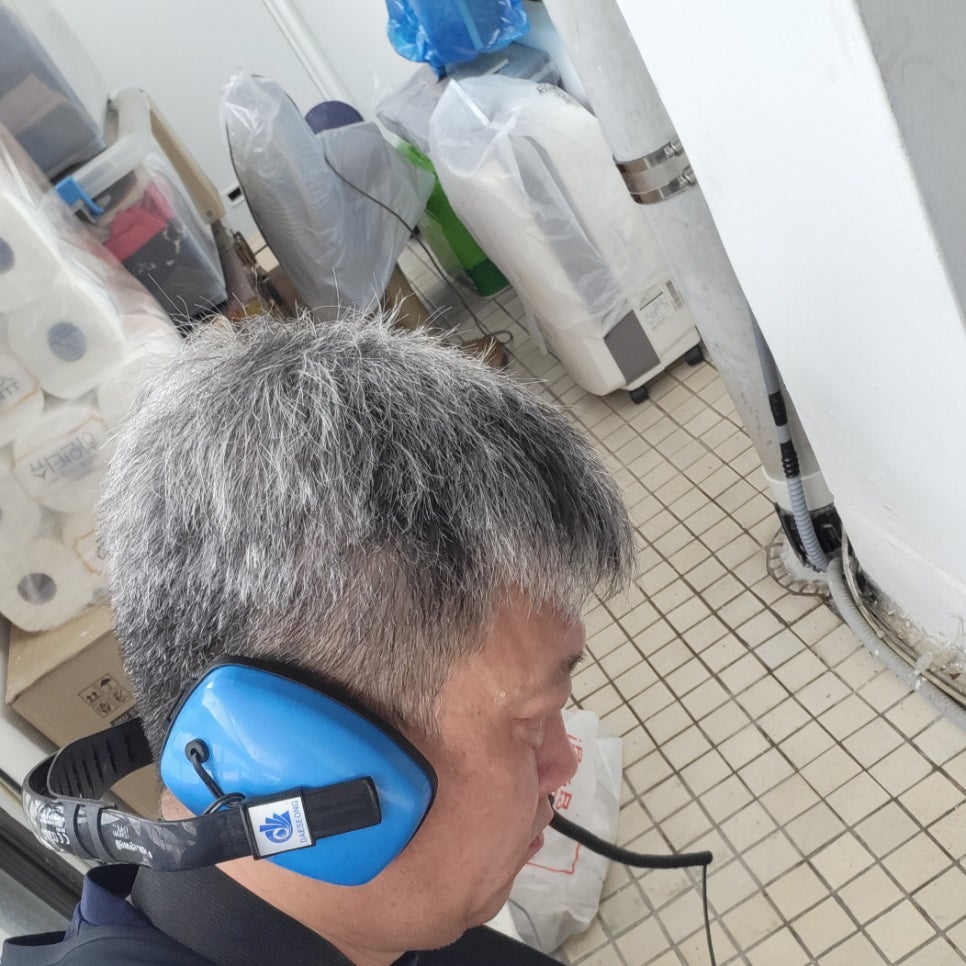 파란 헤드폰을 착용한 작업자와 뒤쪽의 금속 밴드가 둘러진 수직 관