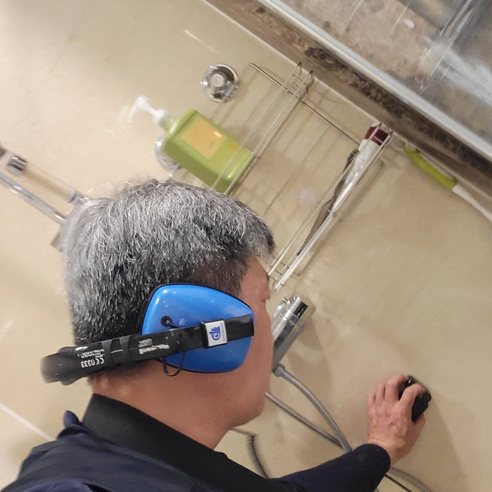 샤워 수전 오른쪽 벽 타일에 검은 장치를 대는 작업자