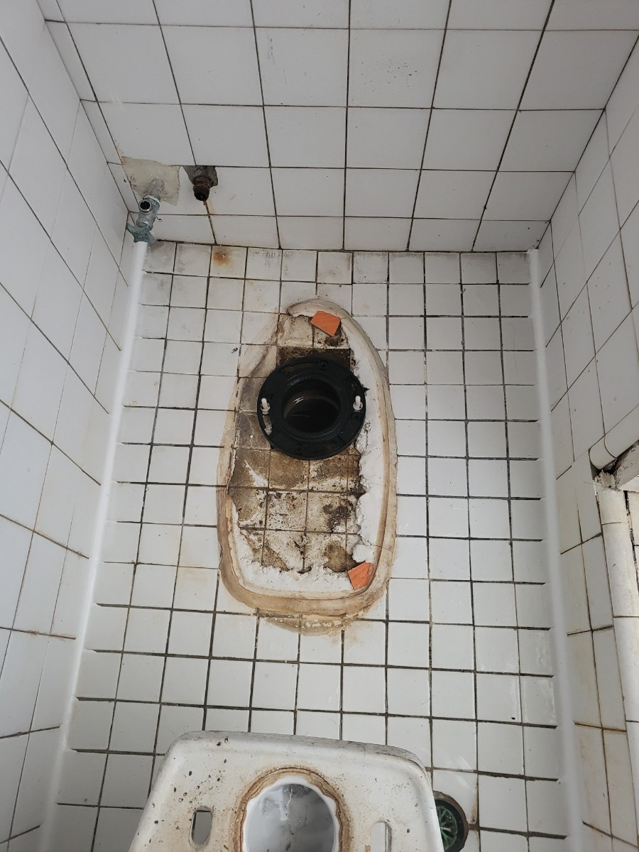 변기를 들어낸 바닥의 검은 배수 연결 부속과 기존 마감 흔적