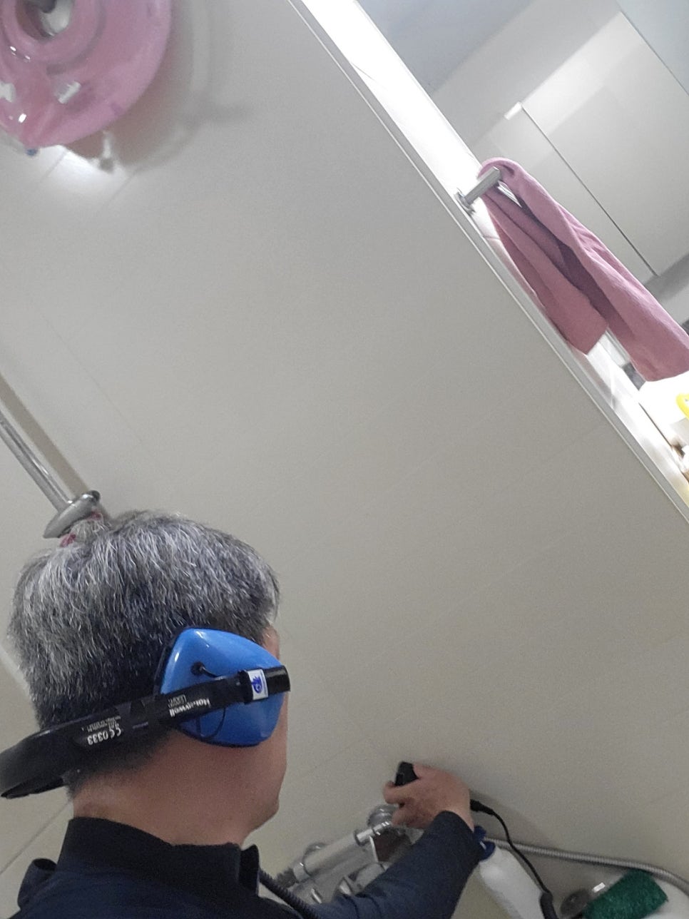 파란 귀덮개를 착용하고 욕실 수전 가까이에 유선 장치를 댄 모습
