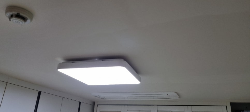 사각 조명과 원형 기기, 길쭉한 천장형 에어컨이 보이는 방 천장