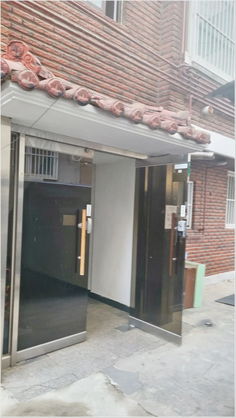 블랙 메탈 중문과 타일 바닥이 자연광 아래에서 모던하게 어우러진 현관이에요.